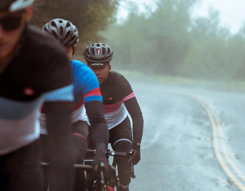 Three cyclists on a wet road with rain gear and helmets.