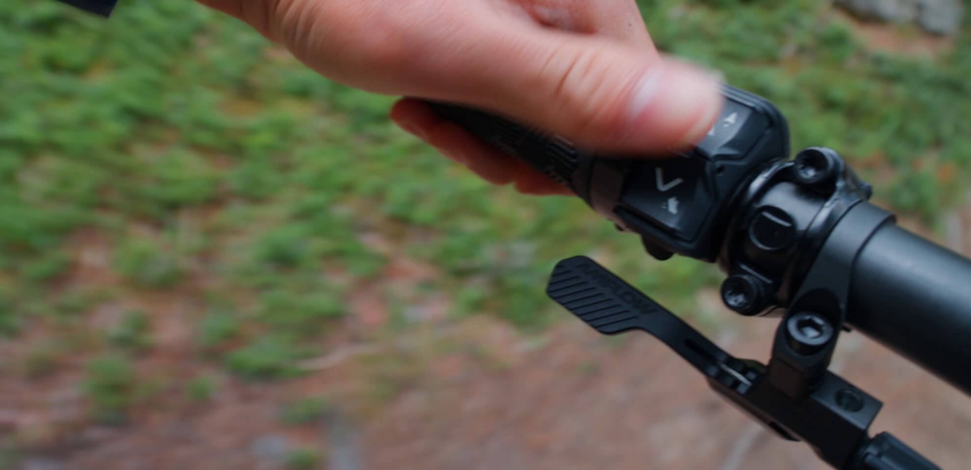 Close-up of a hand pressing an electronic button a bicycle handlebar with a blurred natural background