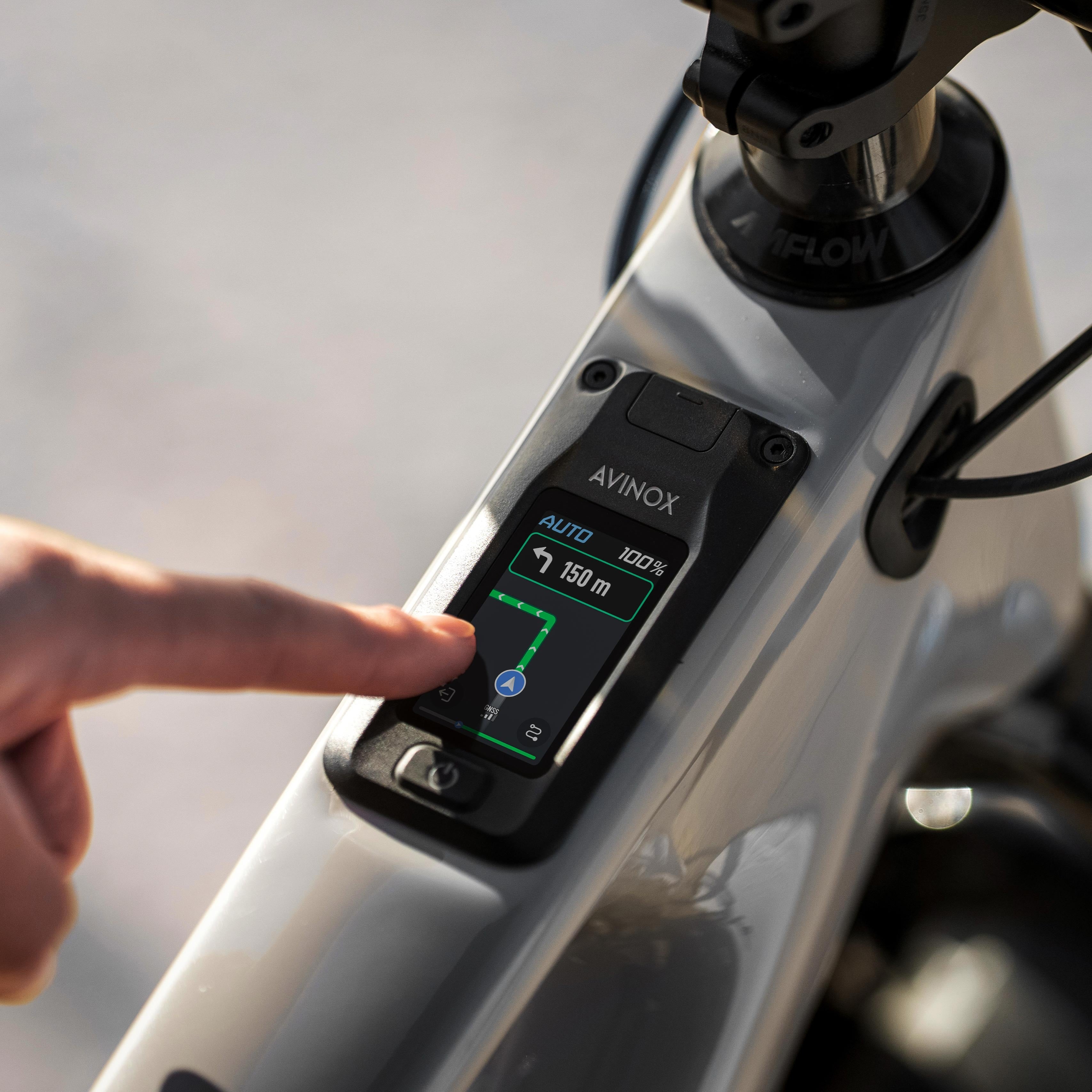 Hand interacting with a digital display on an electric bike, with 'AVINOX' branding.