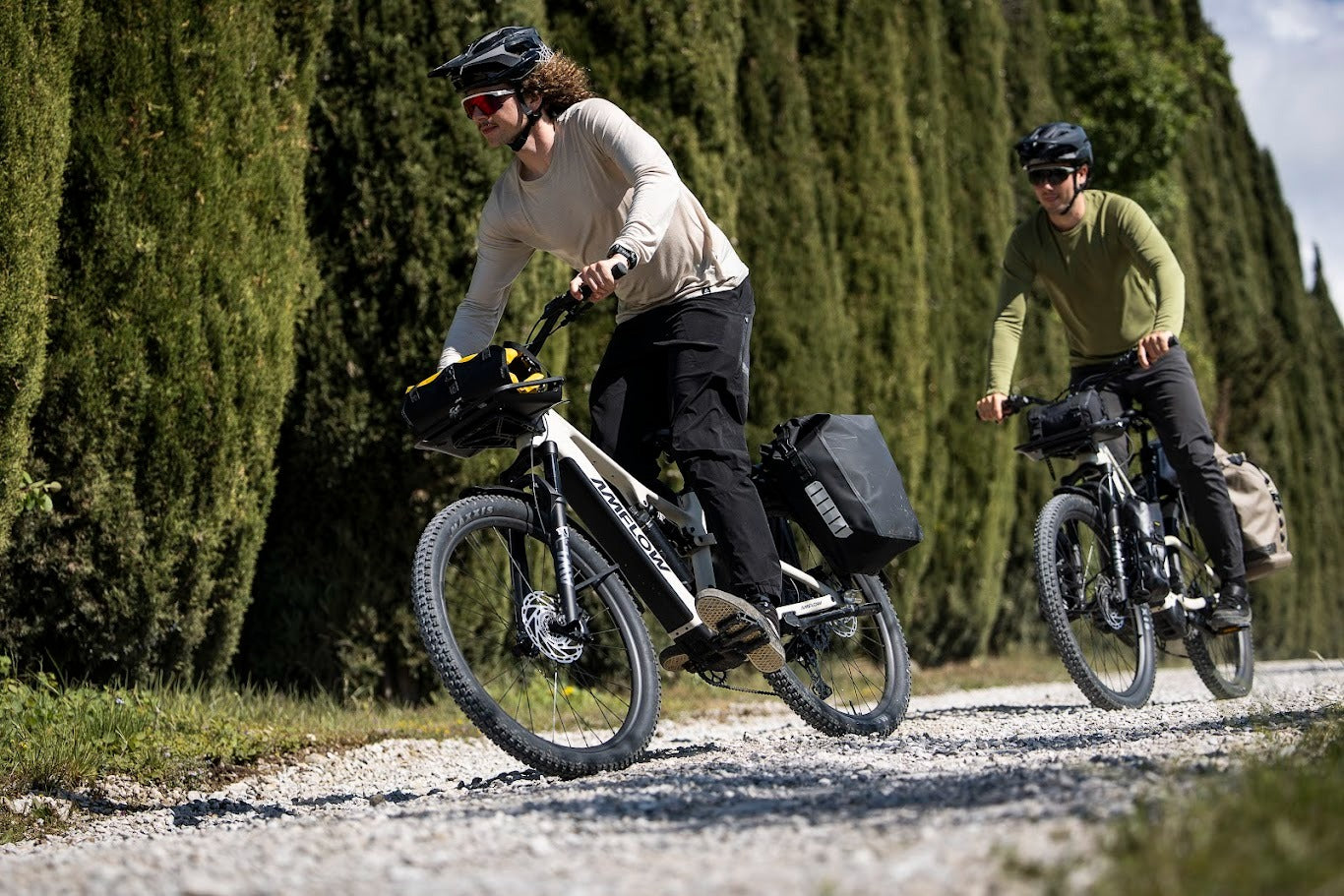 Two people riding Amflow bicycles on a gravel path with greenery in the background
