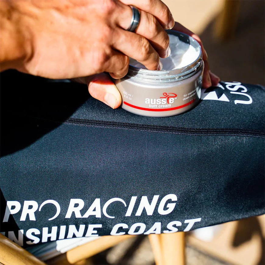 A close up of a hand taking cream out of an Aussie Butt Cream jar on top of a black bag with 'Pro Racing' branding.