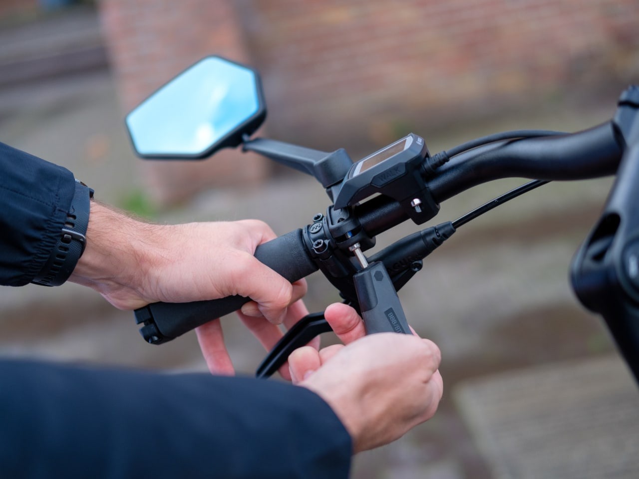 Close-up of a person fitting a bicycle mirror to the handlebar using a tool with a blurred background.