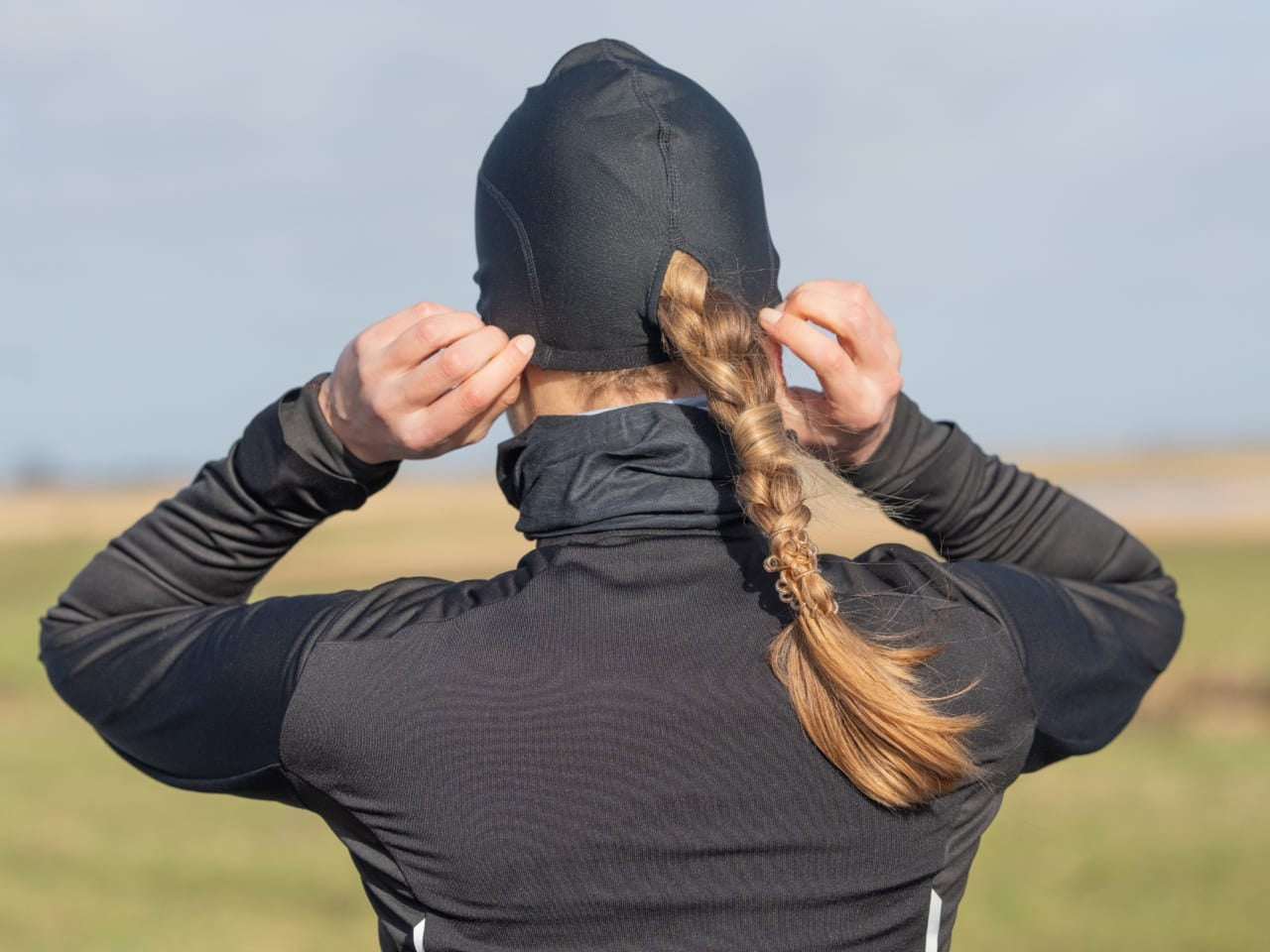 A picture of the back of a woman wearing a thermal skull cap with her plait poking out of the hole at the back