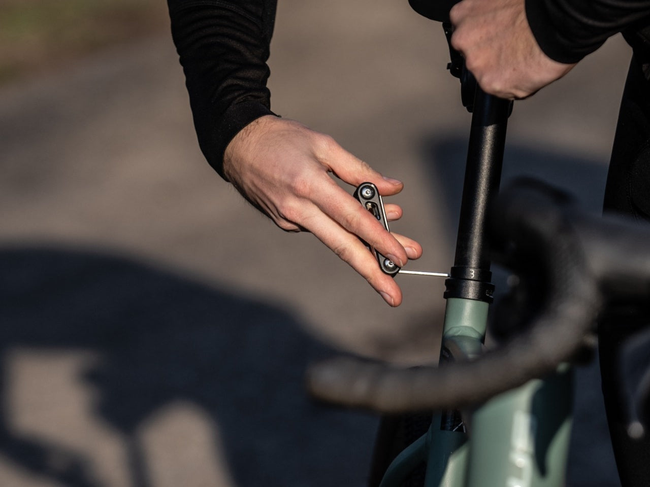 Person adjusting a bicycle seatpost clamp with a tool on a blurred road background