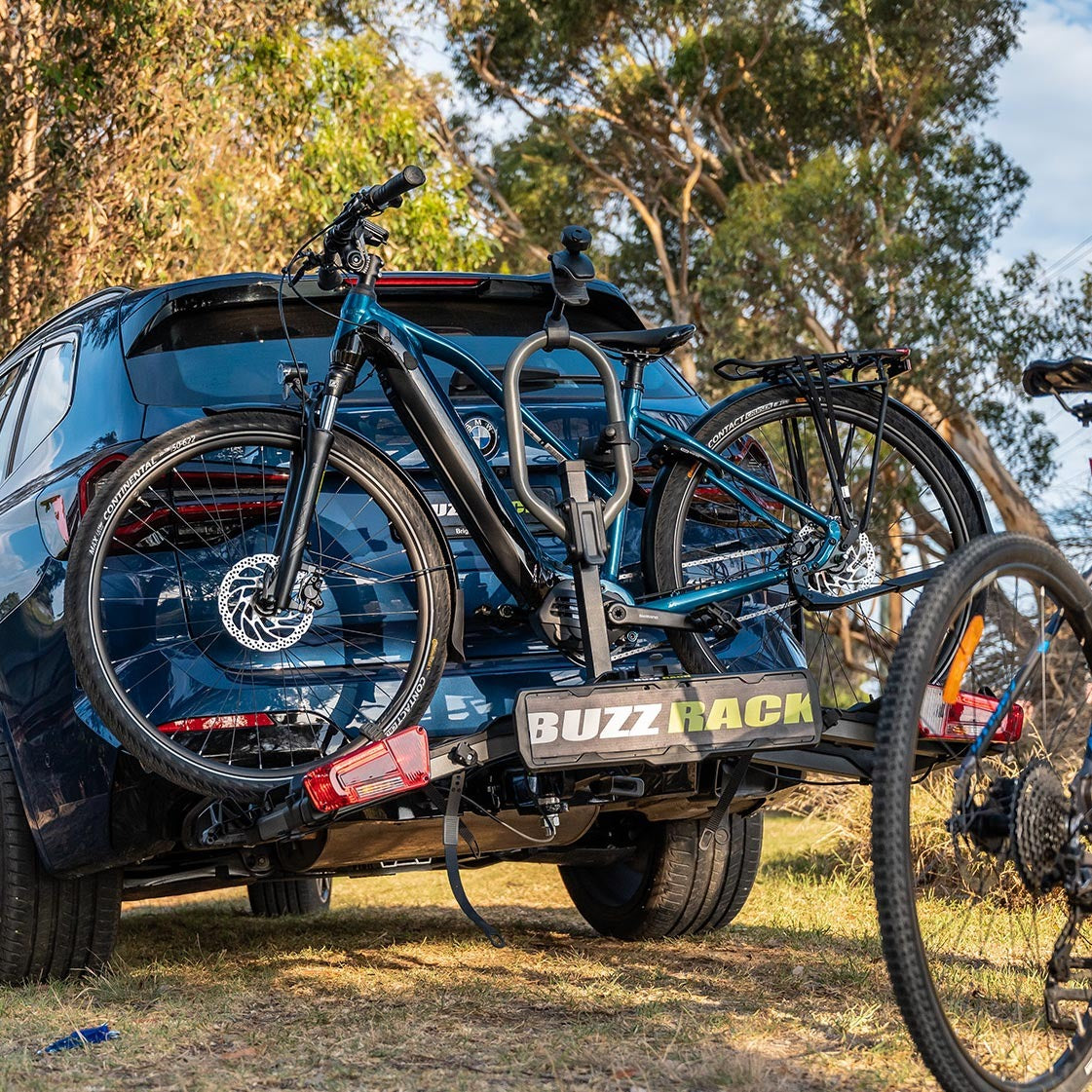 Bicycle on a BuzzRack carrier attached to a blue car in a natural setting.