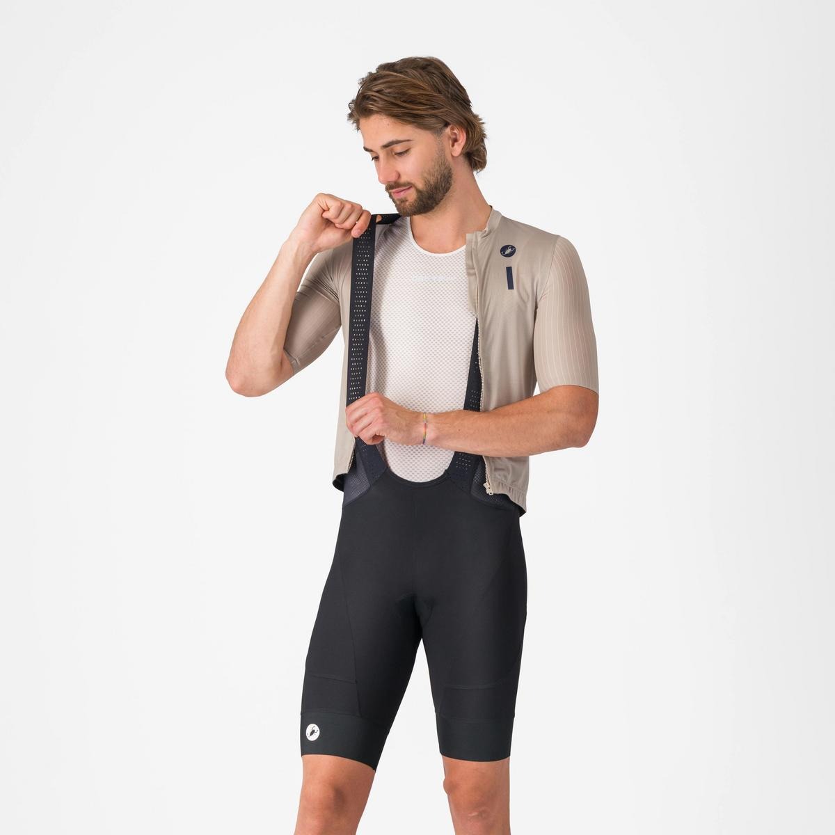 A person wearing cycling bibshorts with jersey unzipped showing the shoulder strap on a light grey background
