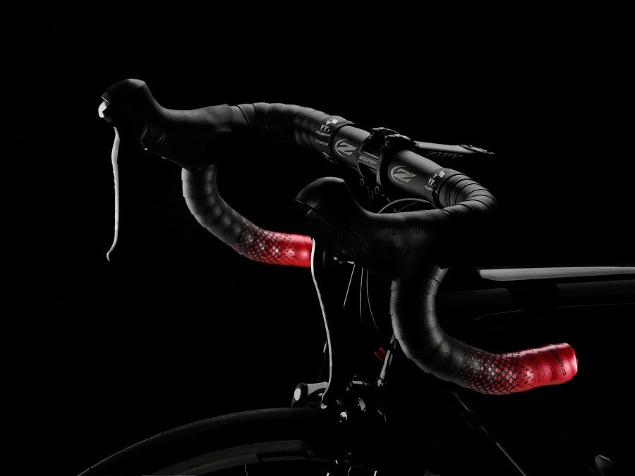 Road bike handlebar with red and black bartape against a black background