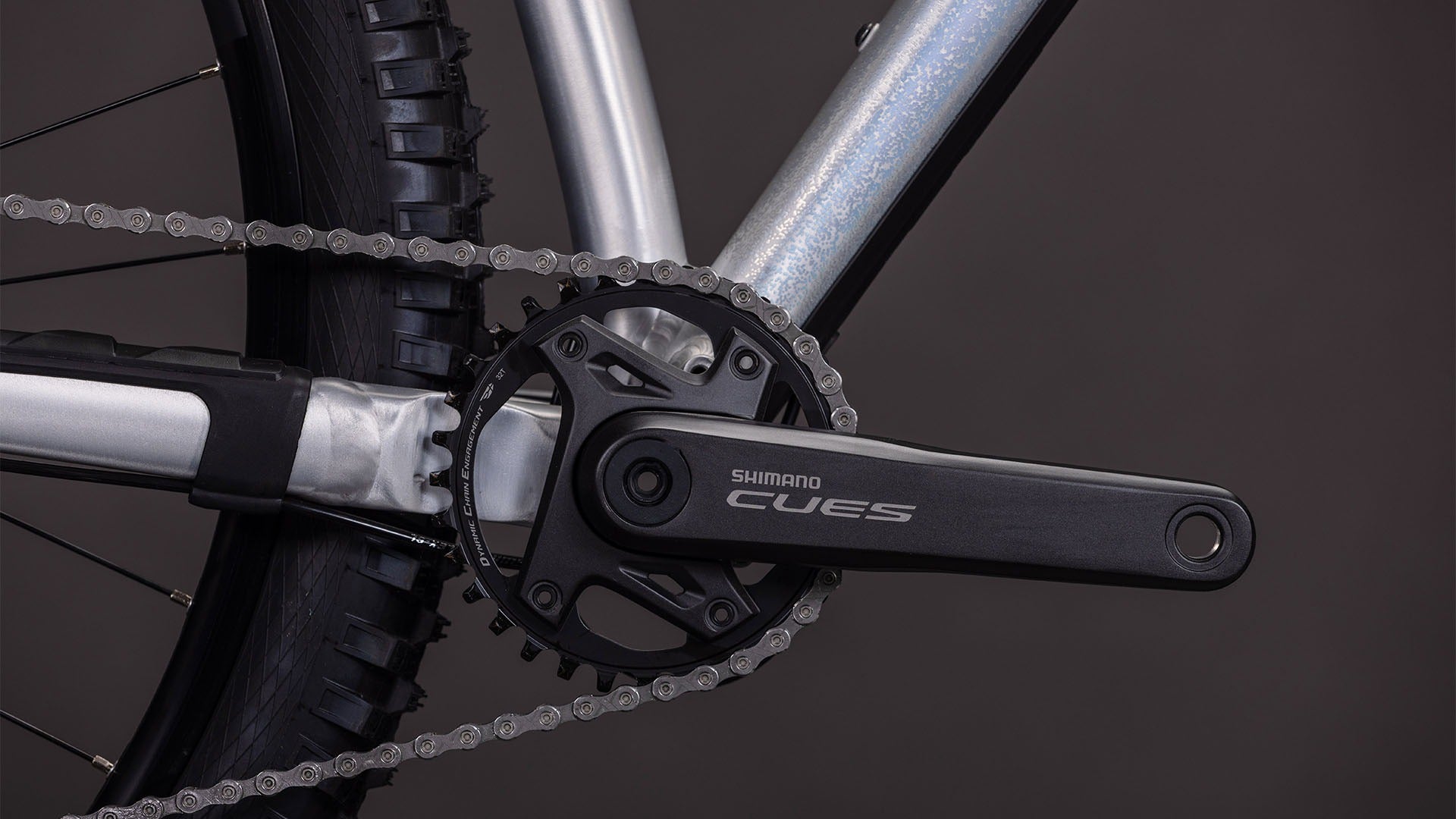 Close-up of a bicycle chain and gear system with 'Shimano CUES' branding on a dark background.