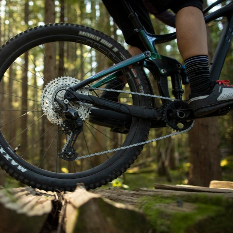 A close up of a drivetrain on a mountain bike being ridden by a person with a forest in the background