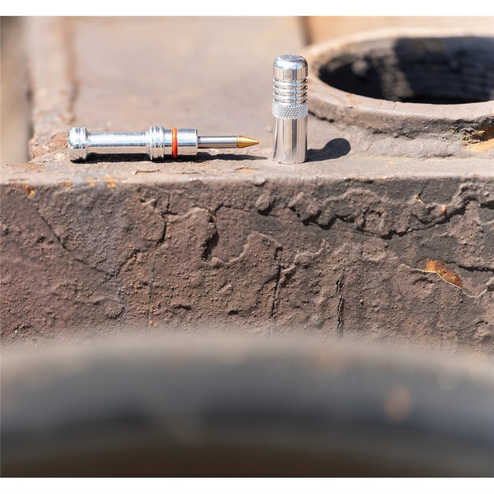 A silver bicycle tubeless repair kit posed ona concrete wall with a blurred bicycle tyre in the foreground