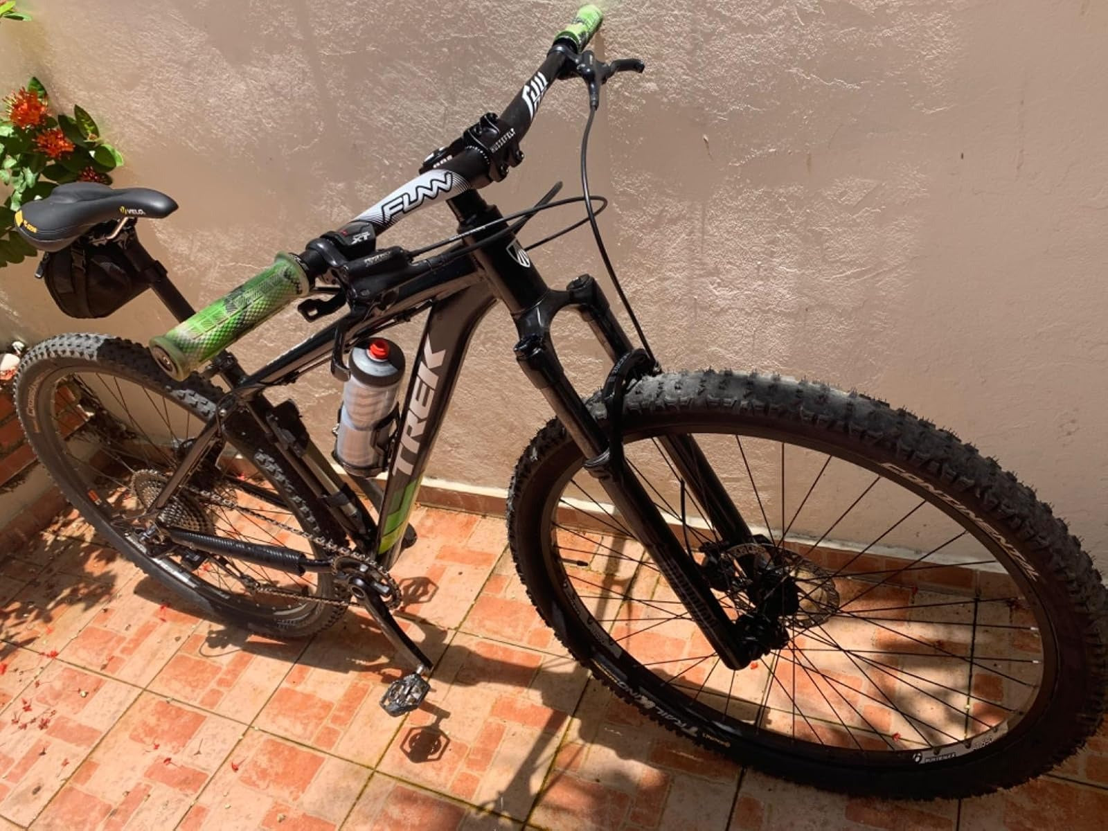 Black mountain bike with green accents on a tiled floor against a beige wall.