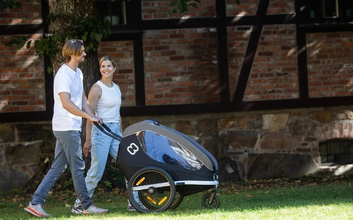 A couple pushing a kids trailer outside in the garden