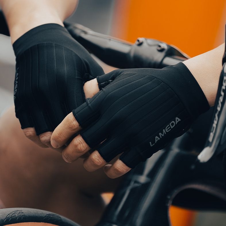 Person wearing black Lameda gloves while leaning on the handlebar of a bike on a blurred background