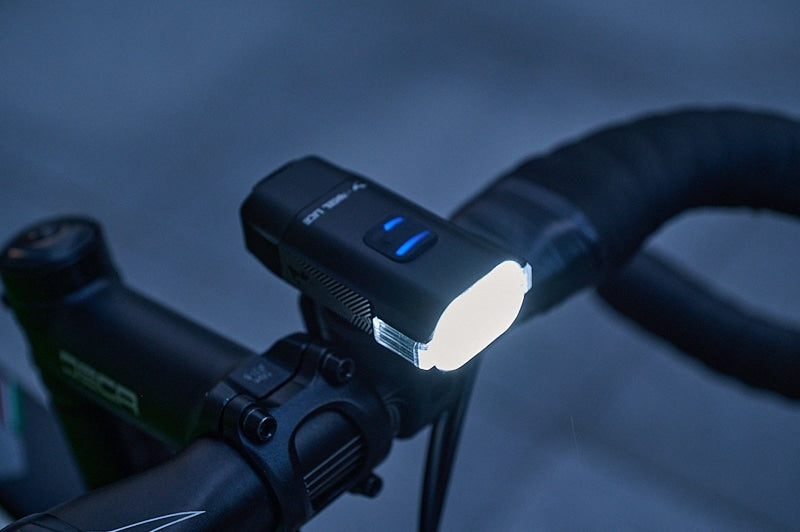 A bright front bicycle light mounted onto road bike handlebars on a dark blue background