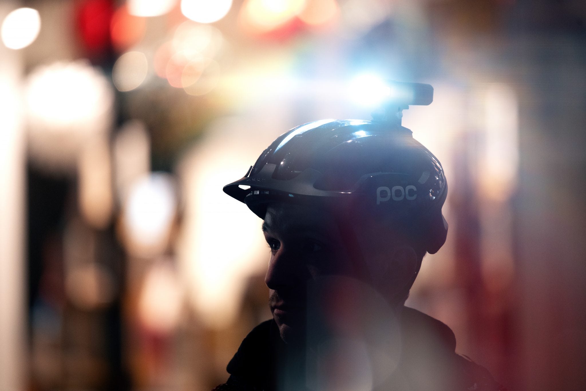 A cyclist with a bright helmet mounted front light with nightlife in the city in the background