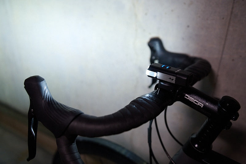 A road bike with a front bright bicycle light mounted on handlebars with a concrete wall in background