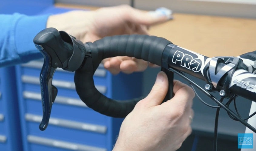 Close-up of a person installing black road bike bar tape with 'PRO' branding.