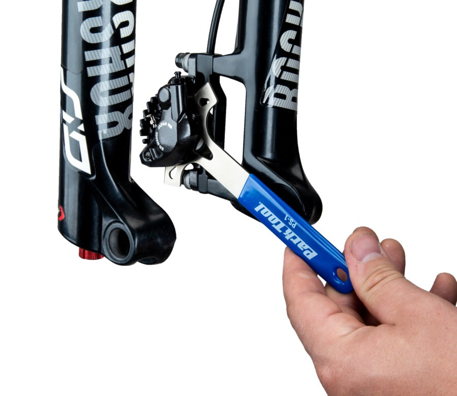 Hand using a Park Tool on a bicycle fork with a white background