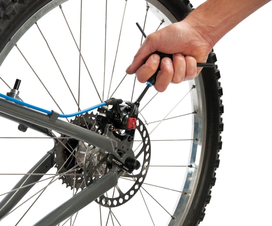 A hand using a three way hex tool on the rear brake calliper on a bike against a white background