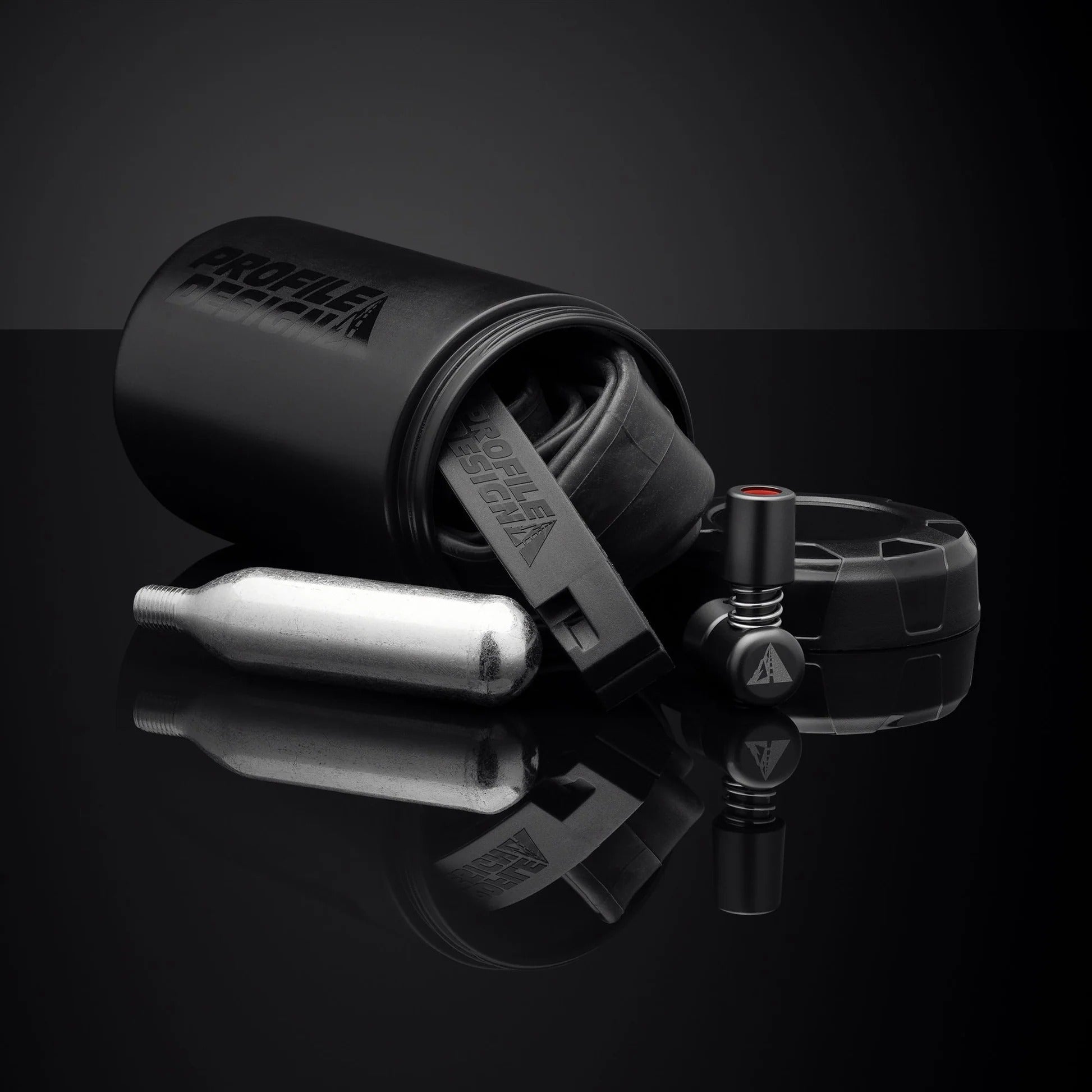 Black bicycle tyre repair kit with tools spilling out of Profile Design storage bottle on a reflective black surface