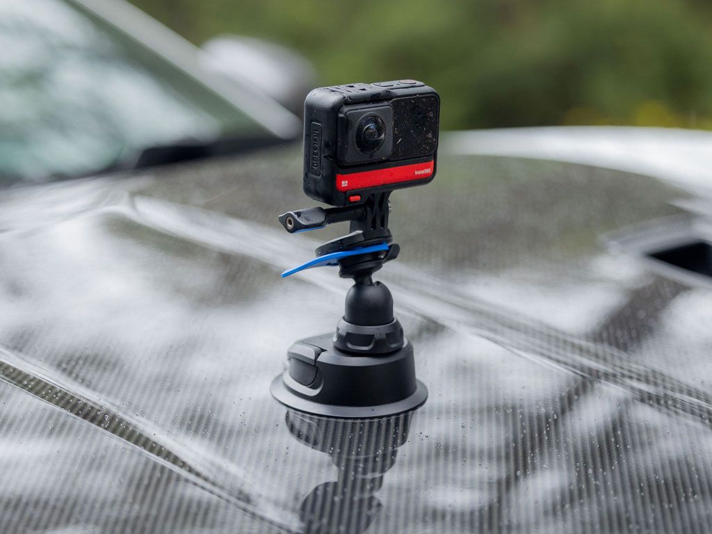 A quad Lock Camera Adapter with camera attached to the hood of a car with a blurred natural background