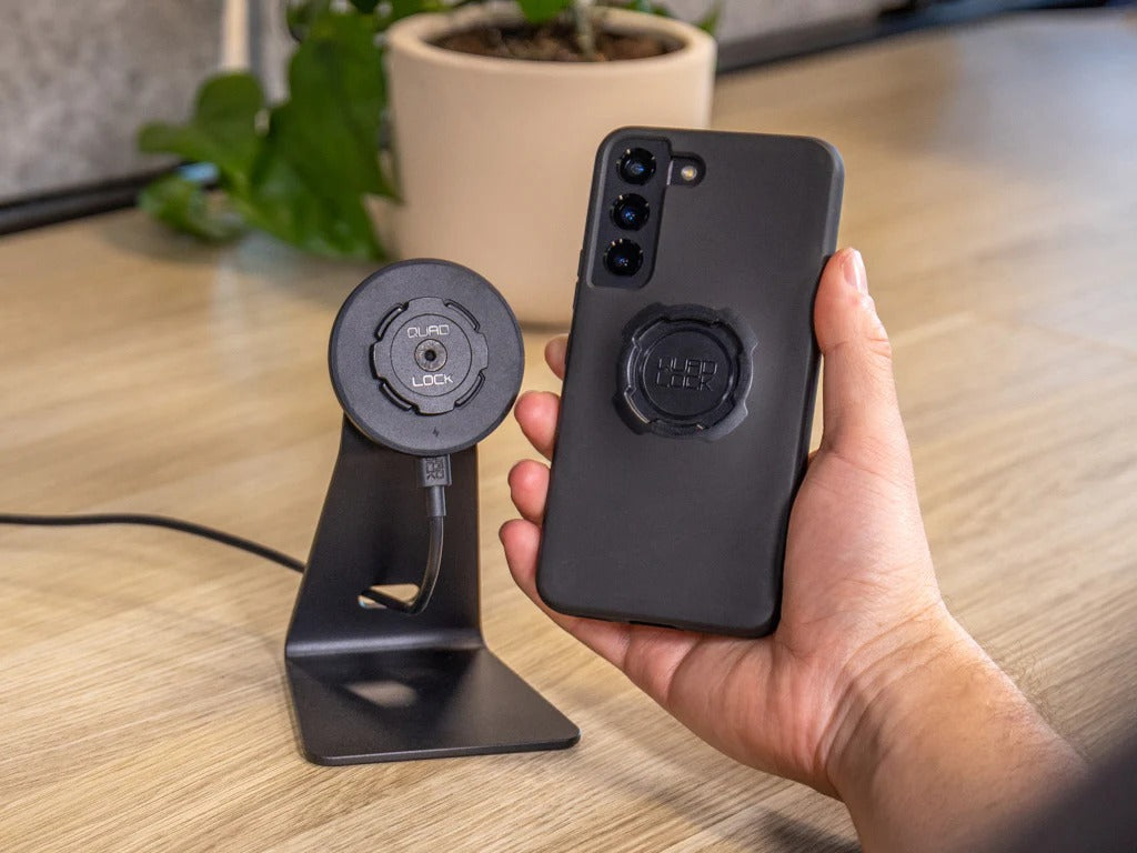 Hand holding a Quad Lock black phone case with a stand on a wooden surface