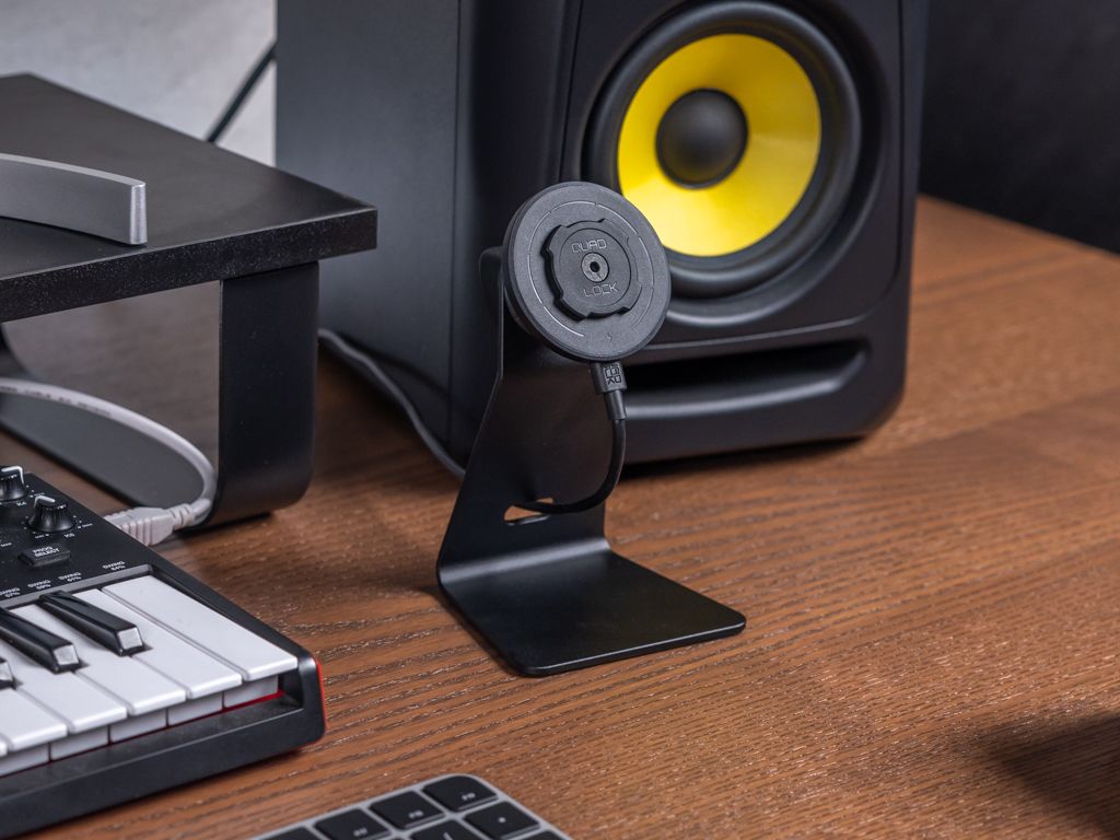 Quad Lock wireless charger on a desk next to a speaker and keyboard