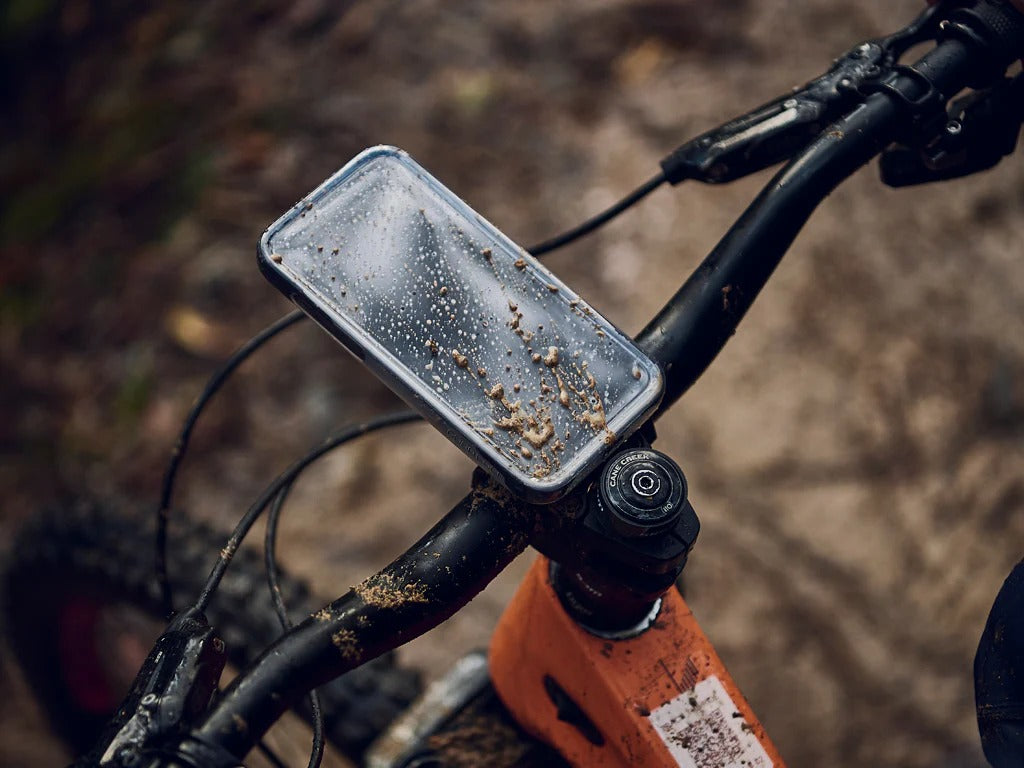 Phone mount on a bicycle handlebar covered in mud splatters with a blurred natural background 