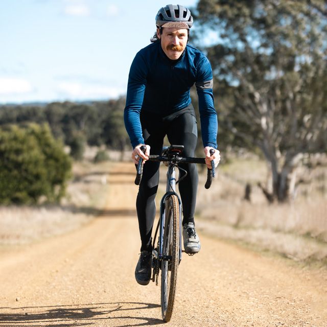 Man riding a gravel bike on a dirt road with trees in the background