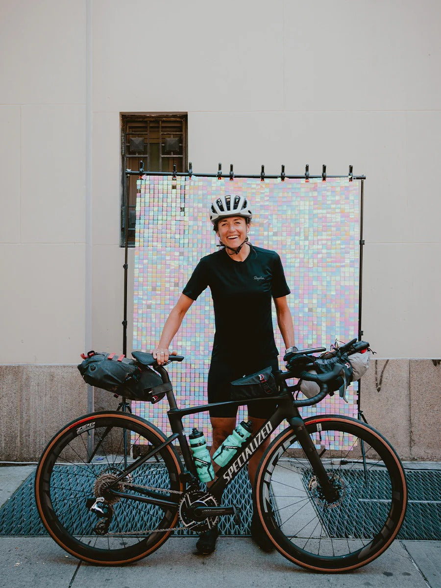 Person standing next to a bicycle with a colorful mosaic wall in the background