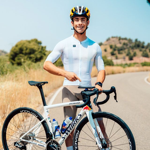 Cyclist in a white jersey with a bicycle on a road with trees in the background