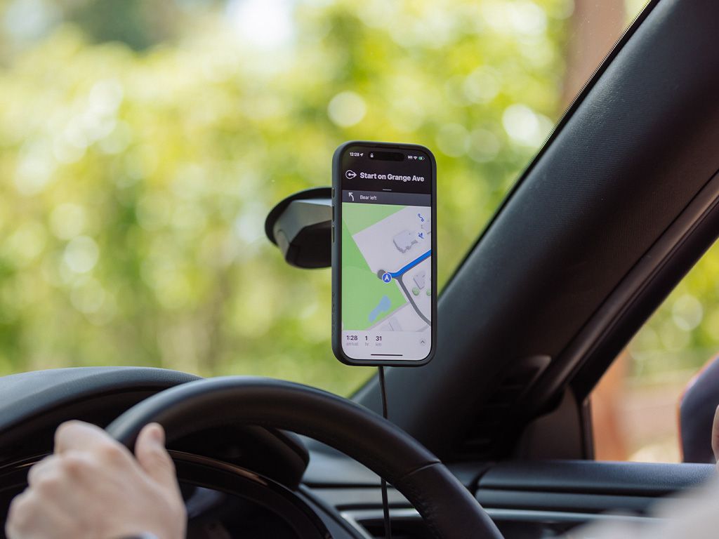 Person driving a car with a smartphone mounted on the dashboard displaying navigation app.