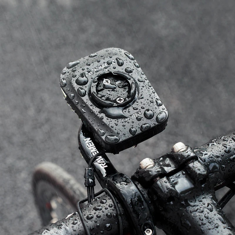 A Ravemen front bicycle light showing rain drops on it and mounted to a road bike with a blurred, rainy background
