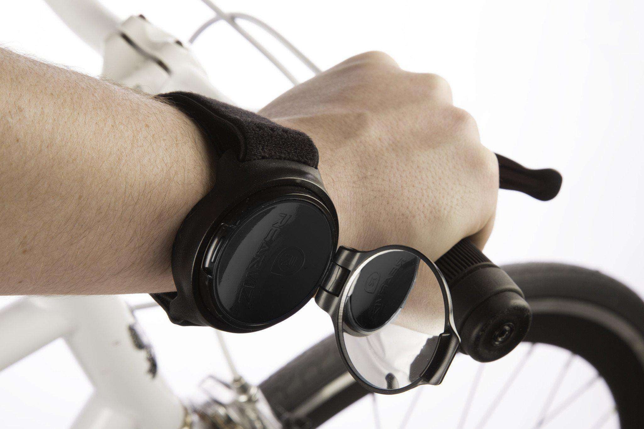 Hand holding a bicycle handlebar with a bicycle mirror attached to wrist on a blurred background