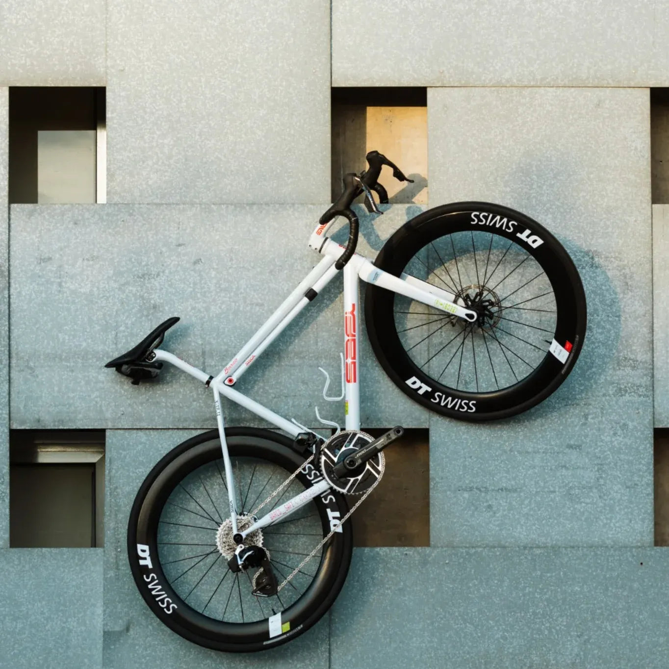 White bicycle leaning against a textured wall with 'DT Swiss' branding on the wheels.