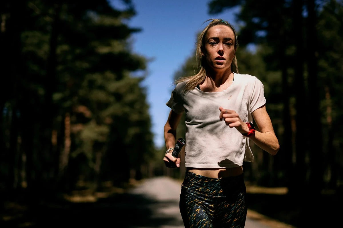 Woman running on a path in a forest holding a SIS Beta Fuel Gel in her hand