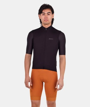 Person wearing a black cycling jersey, black vest and orange shorts on a white background