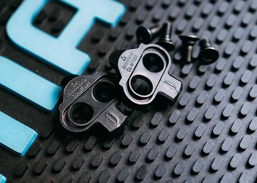 Two Shimano SPD Mountain Bike Cleats against a black textured rubber surface