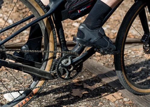 Close-up of a person riding a bicycle on a gravel path wearing cycling sandles