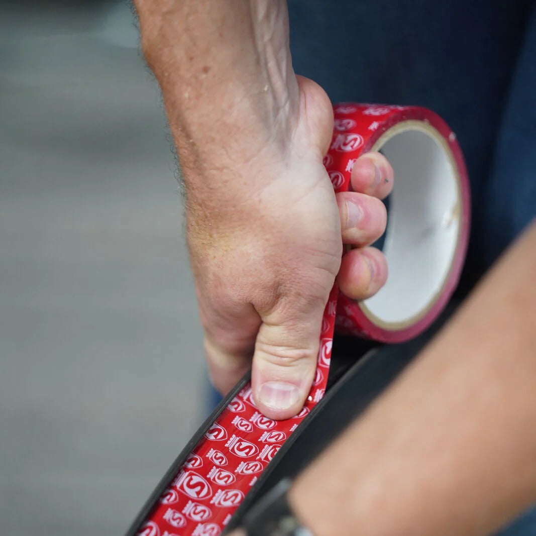 Hand applying red tubeless rim tape with a pattern to a bicycle wheel.