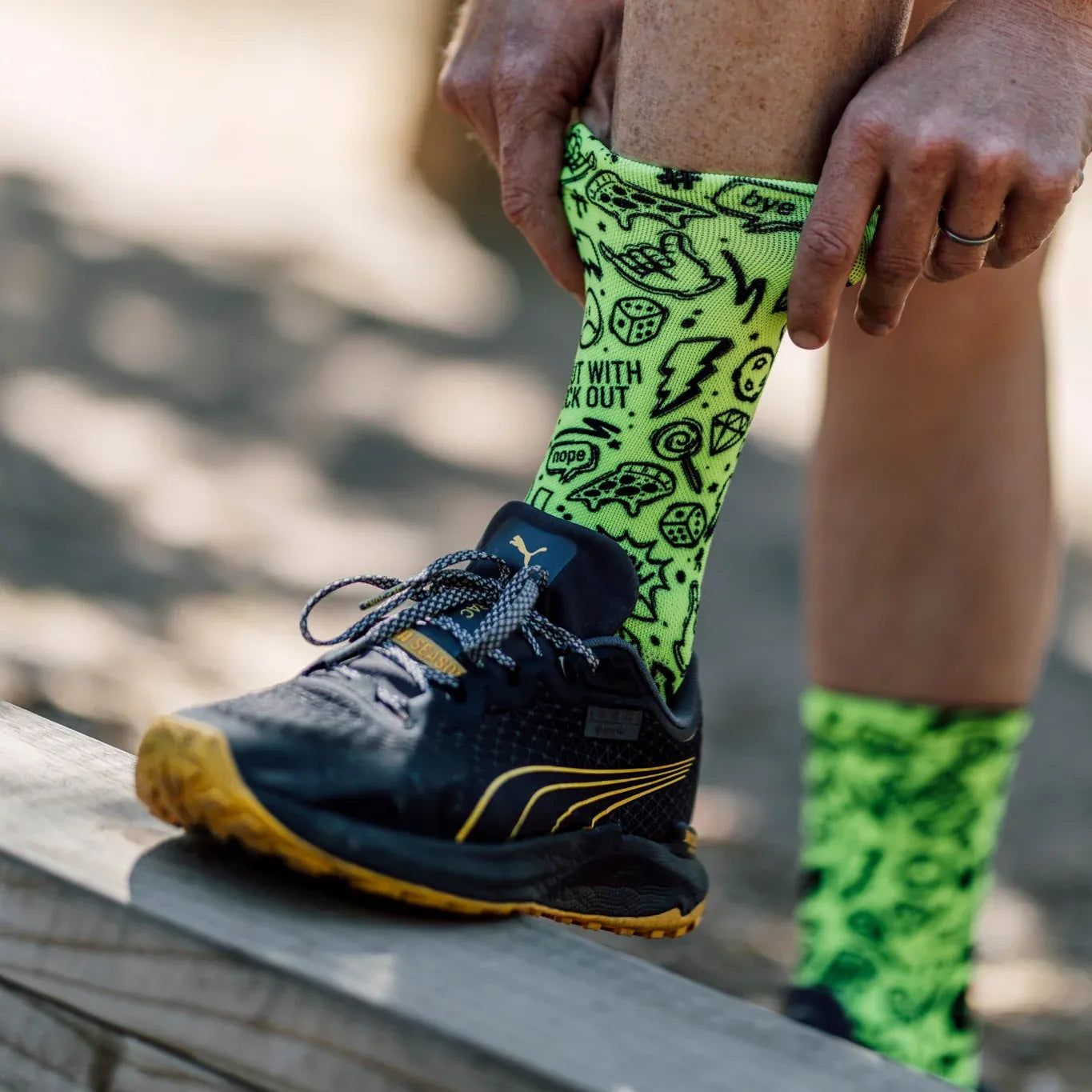 Person wearing green patterned socks with black text and a black athletic shoe on a blurred background