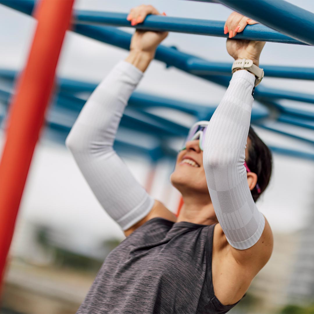 A picture of a women doing a pull up and wearing the Sox Slight White Arm Sleeves