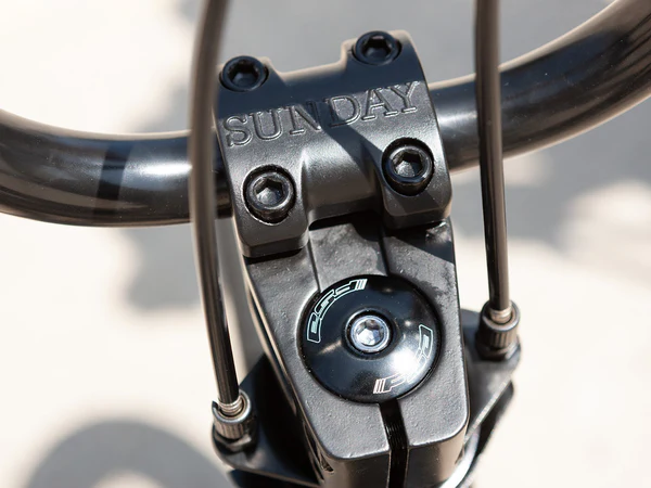 Close-up of a bicycle handlebar stem with 'SUNDAY' branding on a blurred background