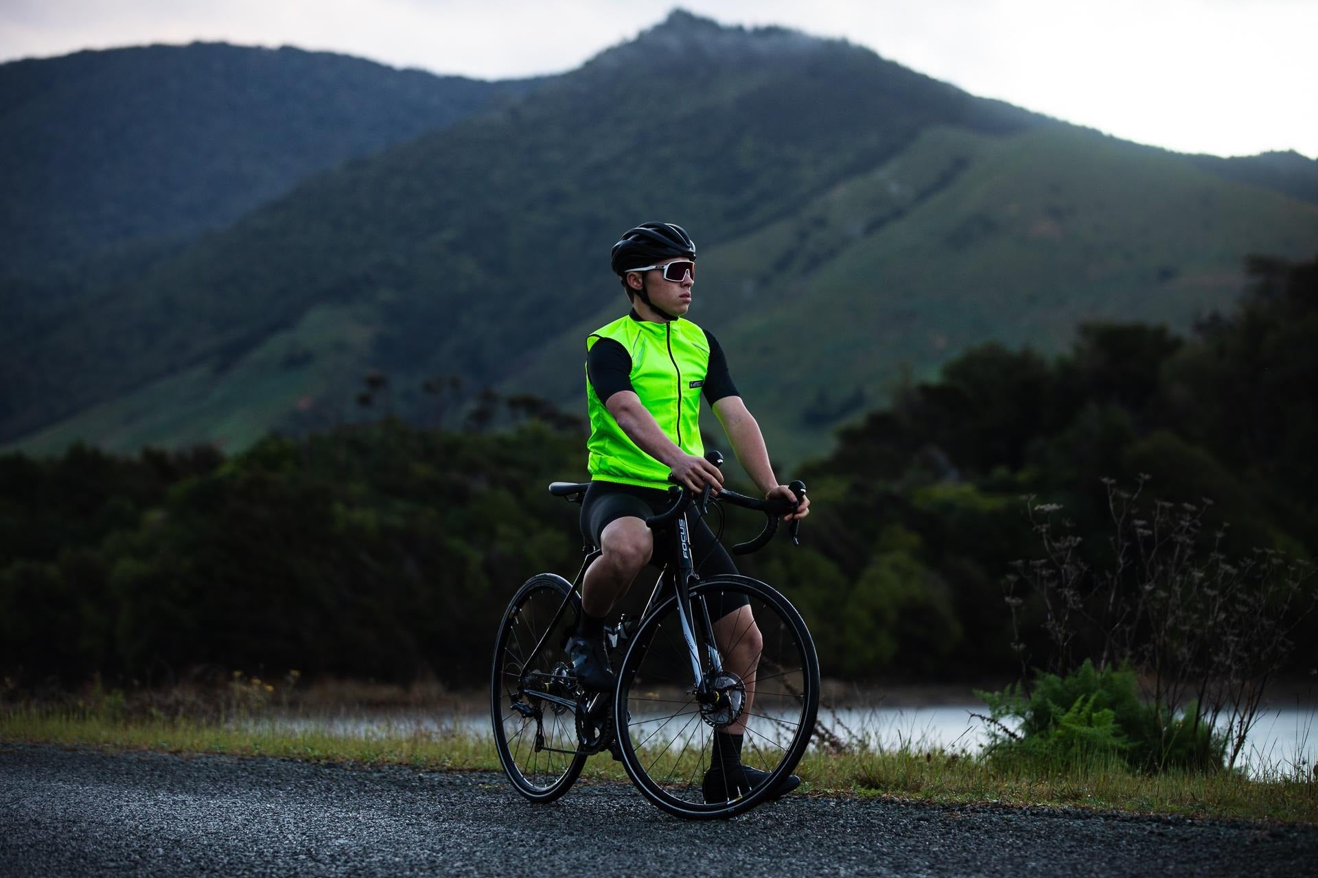 Cyclist in a bright green vest riding on a road with mountains in the background