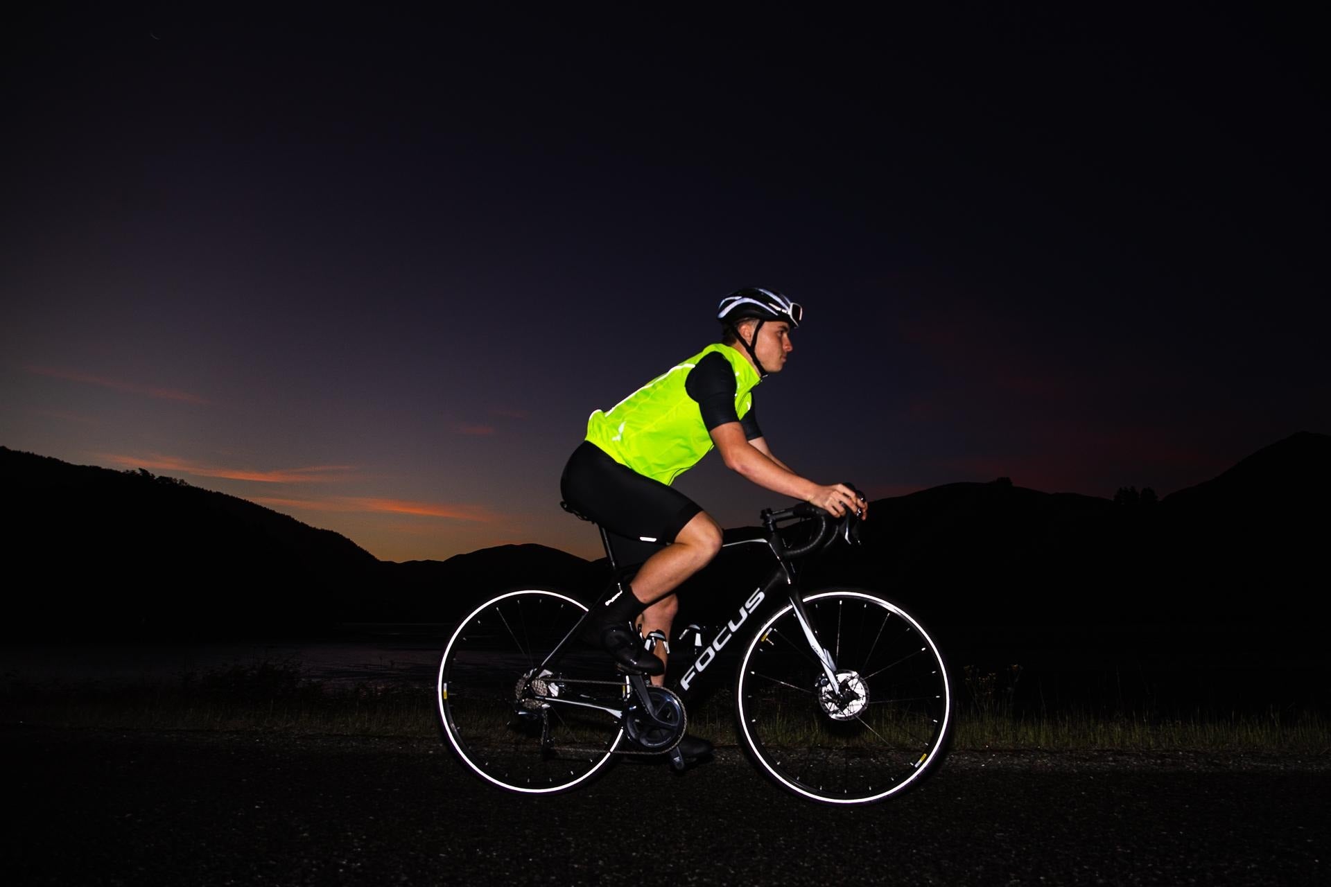 Cyclist on a dark road wearing a bright yellow vest and helmet.