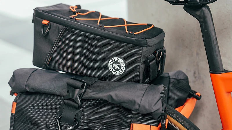 Black and orange bicycle pannier bags mounted to a bikewith a visible brand logo on a gray background