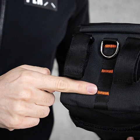 Person pointing to a black pannier bag with orange accents.