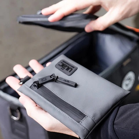 Person holding a gray wallet in one hand and opening a pannier bike bag with the other hand