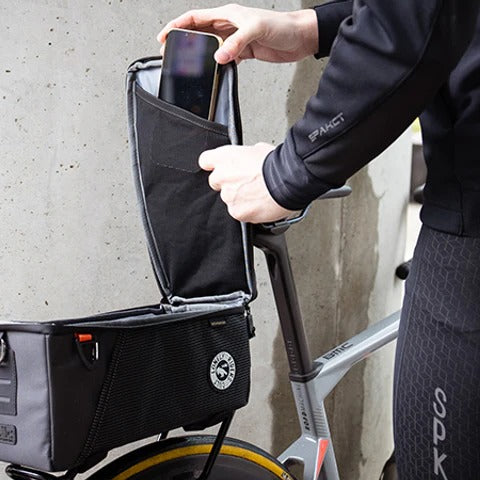 Person storing phone into a black bike pannier bag with a concrete wall background