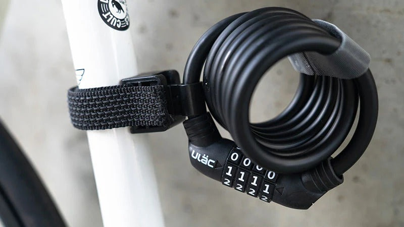 Black bicycle lock with a combination dial attached to a white bike frame.